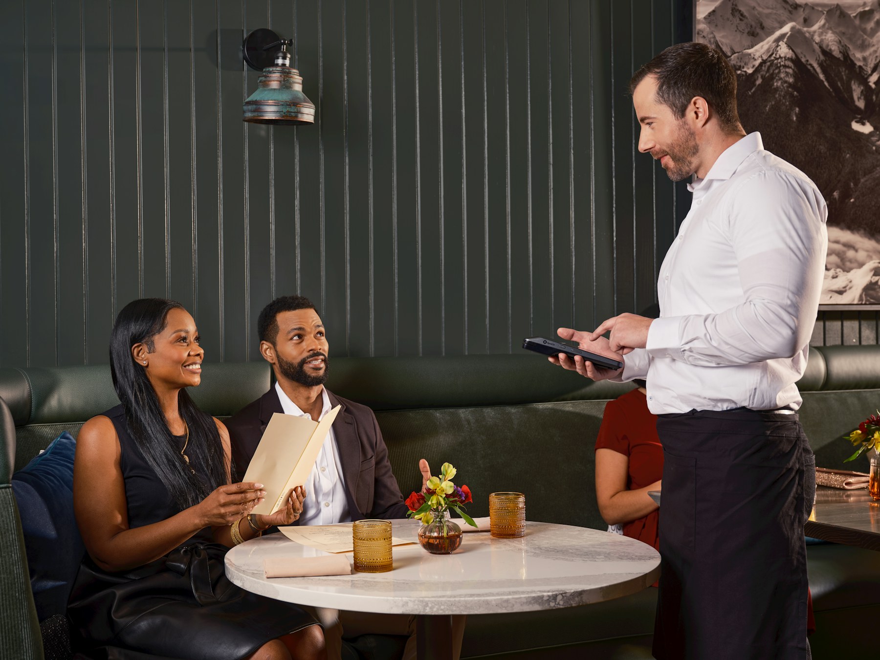 Waiter using hospitality technology while assisting guests at their table